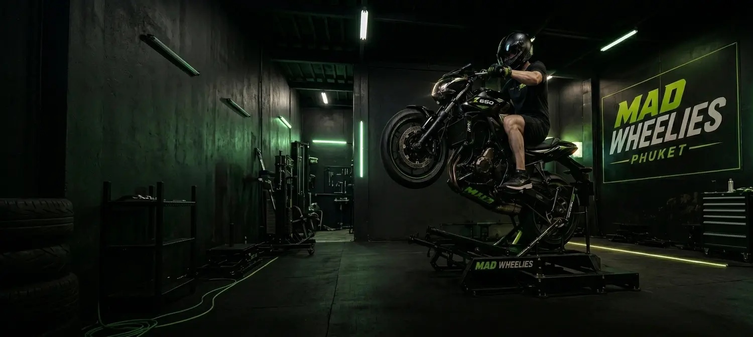 A rider performing a wheelie on a Kawasaki Z650 on the Mad Wheelies training rig at their Phuket studio, with Mad Wheelies Phuket branding on the wall