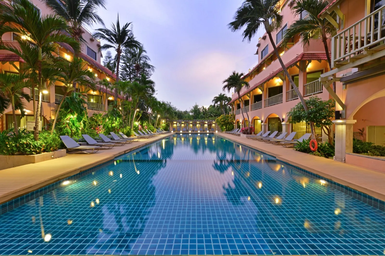 Long swimming pool lined with sunbeds and palms at dusk at Anantasila Beach Resort Hua Hin