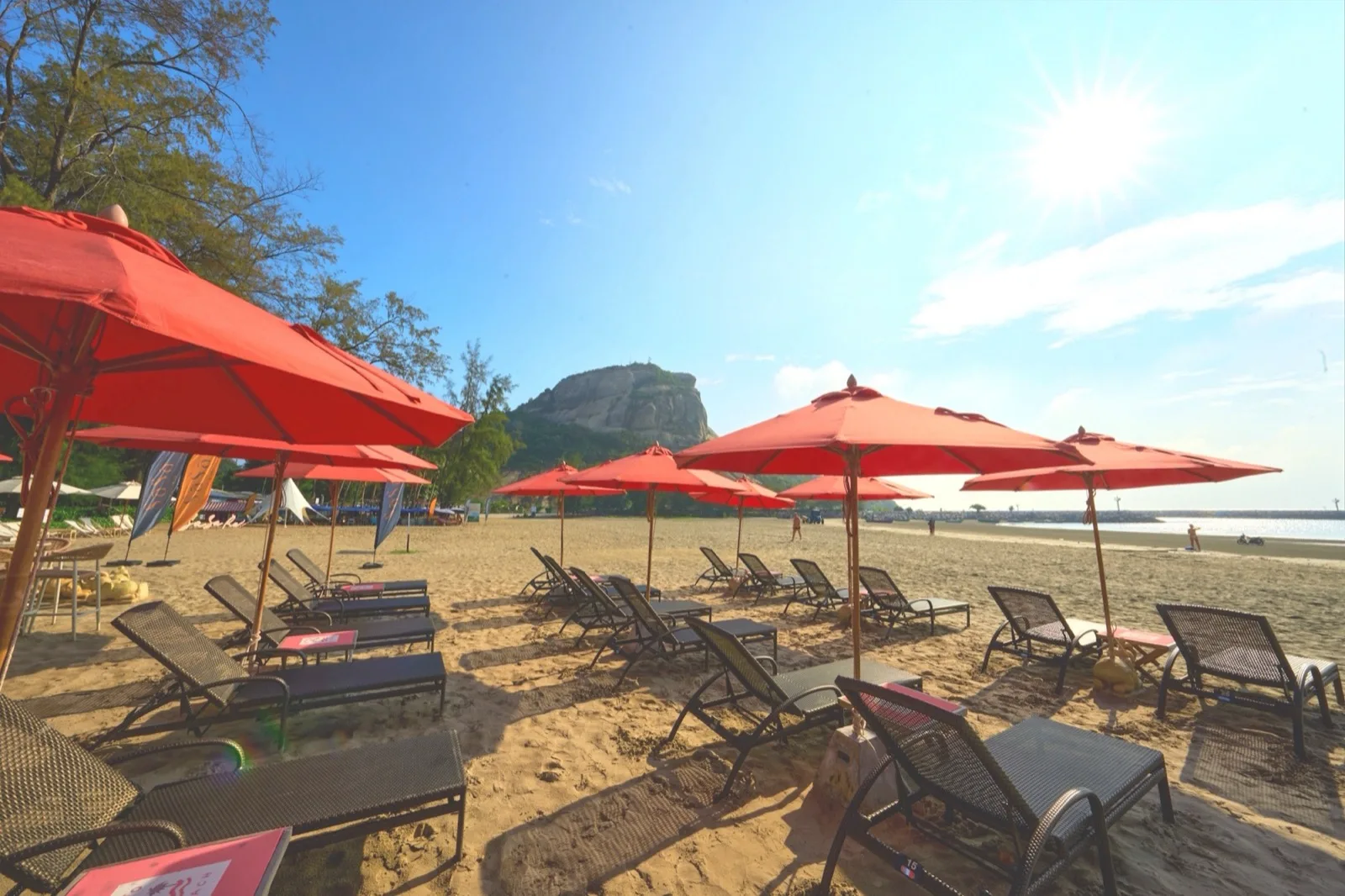 Red umbrellas and sunbeds on Hua Don Beach with Khao Takiab hill behind, Anantasila Hua Hin