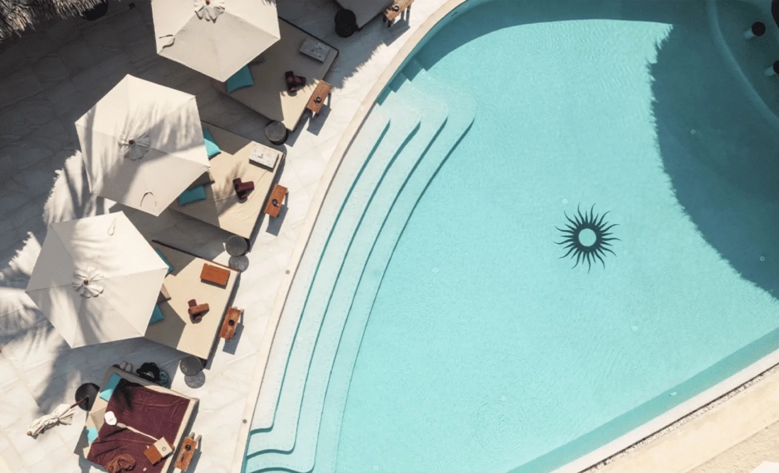 Aerial view of pool deck beds and umbrellas beside the turquoise pool at Carpe Diem Beach Club