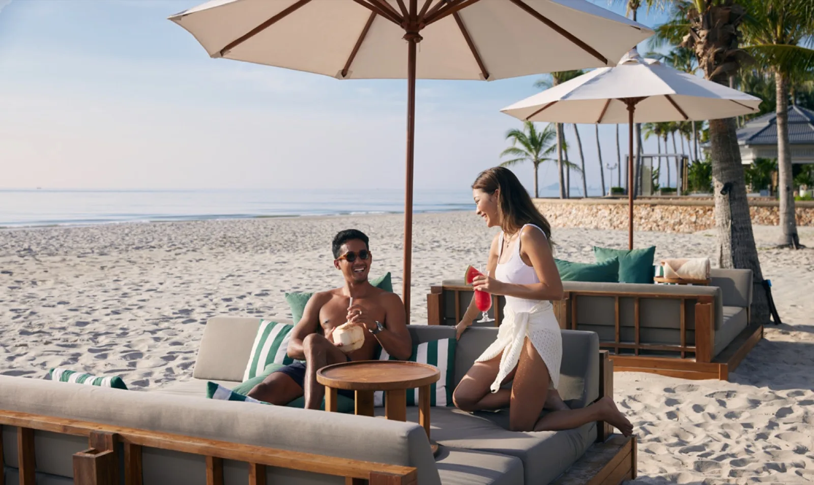 Couple relaxing on beach lounge sofas under umbrellas at Dusit Thani Hua Hin