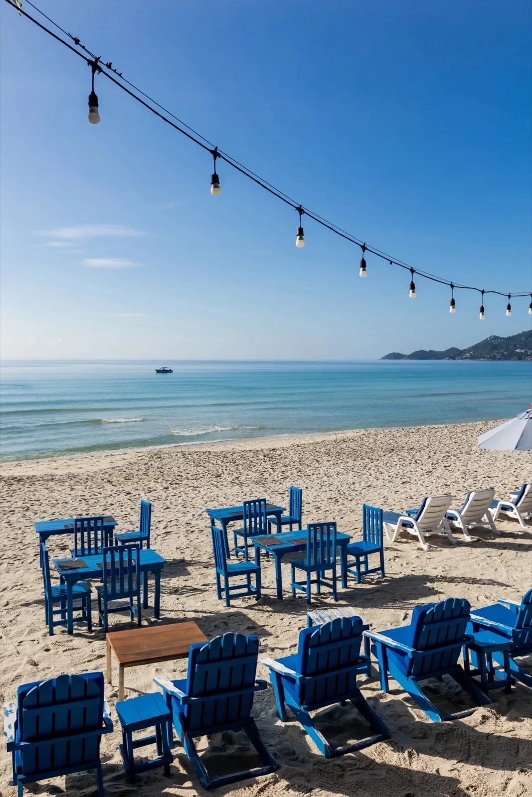 Blue beach chairs and tables under string lights on Chaweng Beach at Malibu Beach Resort Samui