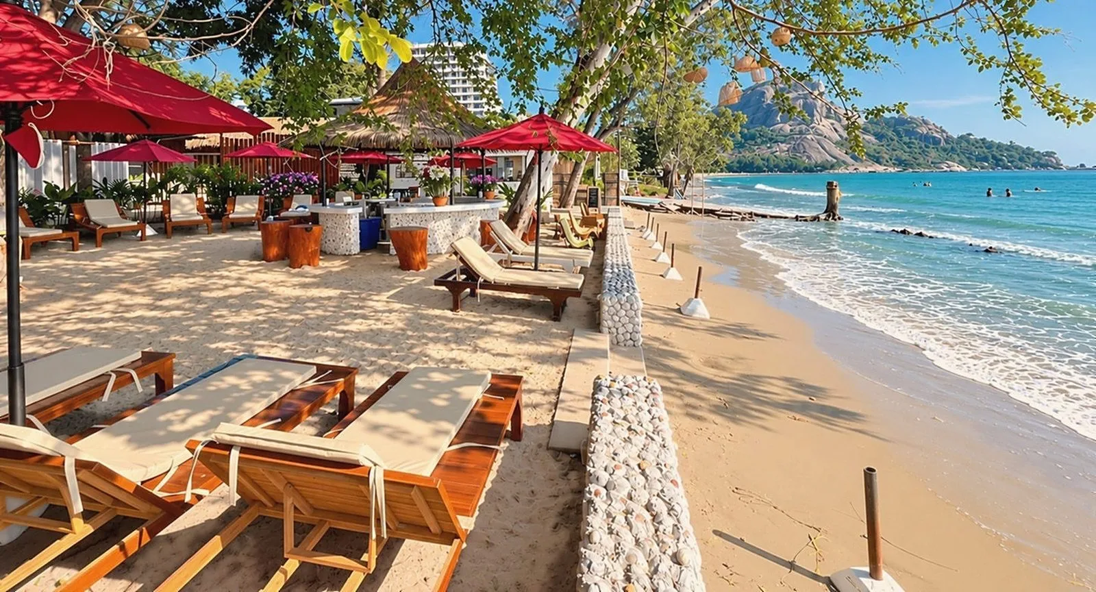 Loungers along the shore with Khao Takiab hill in the distance at Mama Daeng Beach Sauna