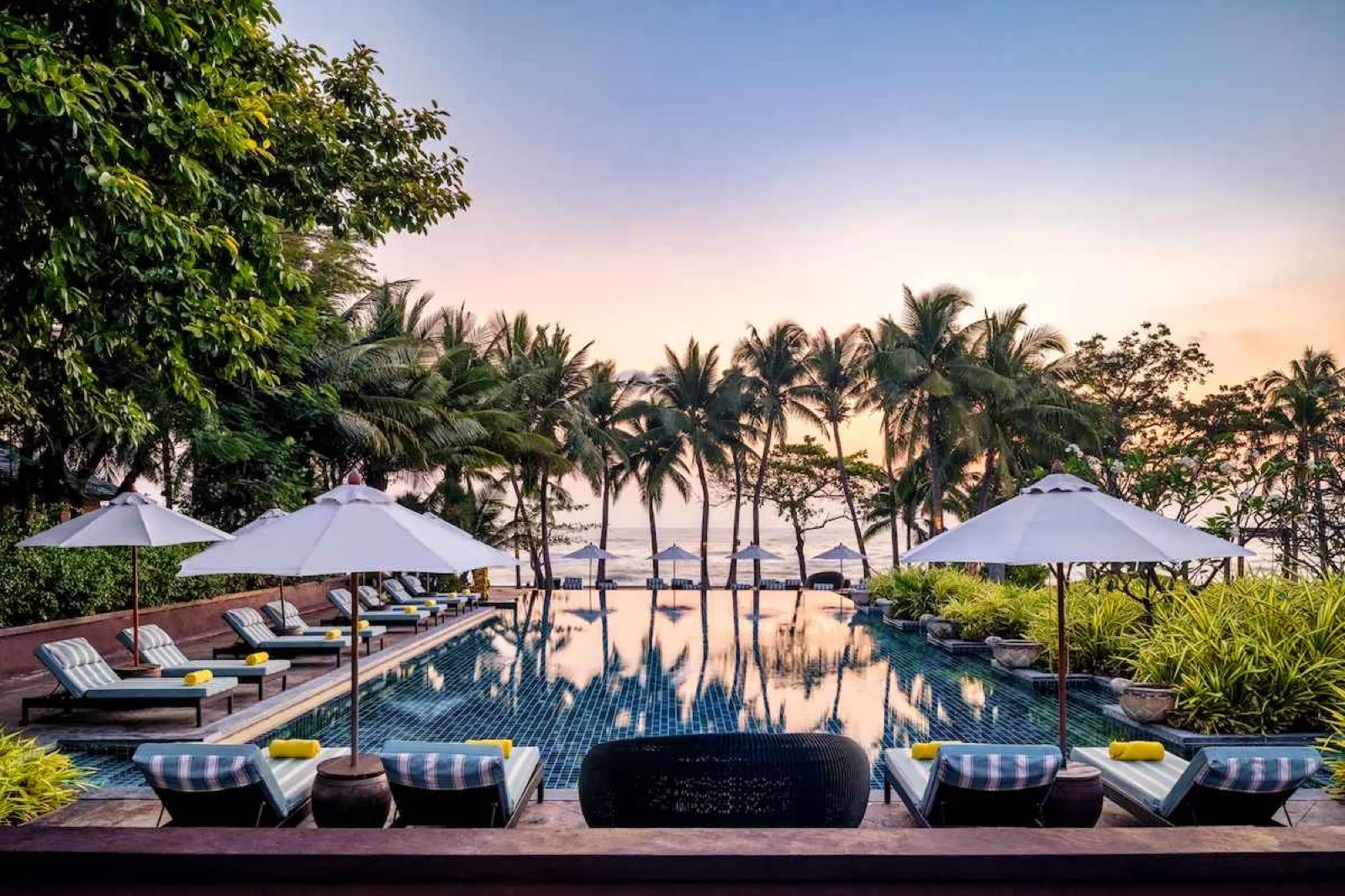 Infinity pool with loungers and umbrellas at sunset at Mövenpick Asara Resort and Spa Hua Hin