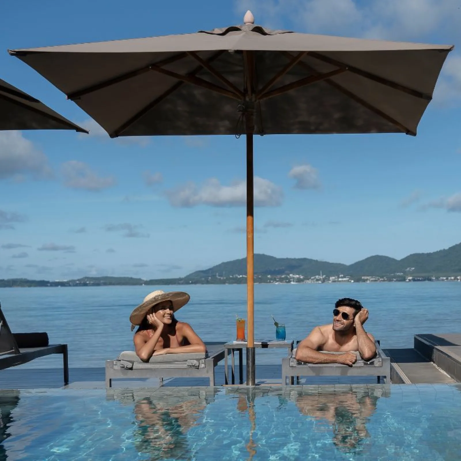 Couple relaxing by the infinity pool at My Beach Resort Phuket overlooking Ao Yon bay