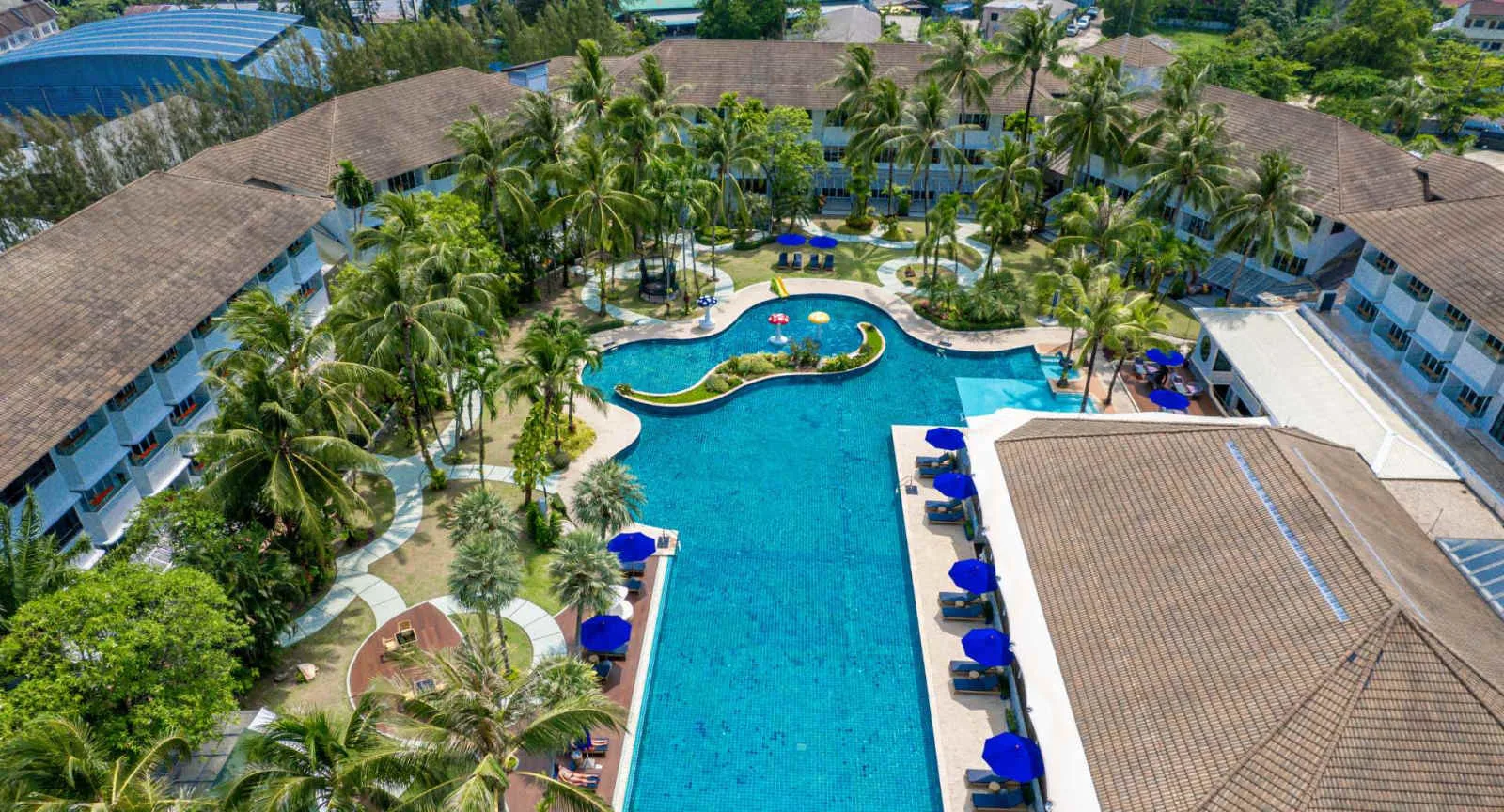 Aerial view of the 50 metre pool at NH Boat Lagoon Phuket Resort surrounded by palms and blue umbrellas