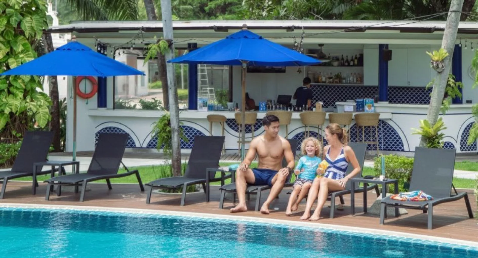 Family relaxing on the pool deck by the poolside bar at NH Boat Lagoon Phuket Resort