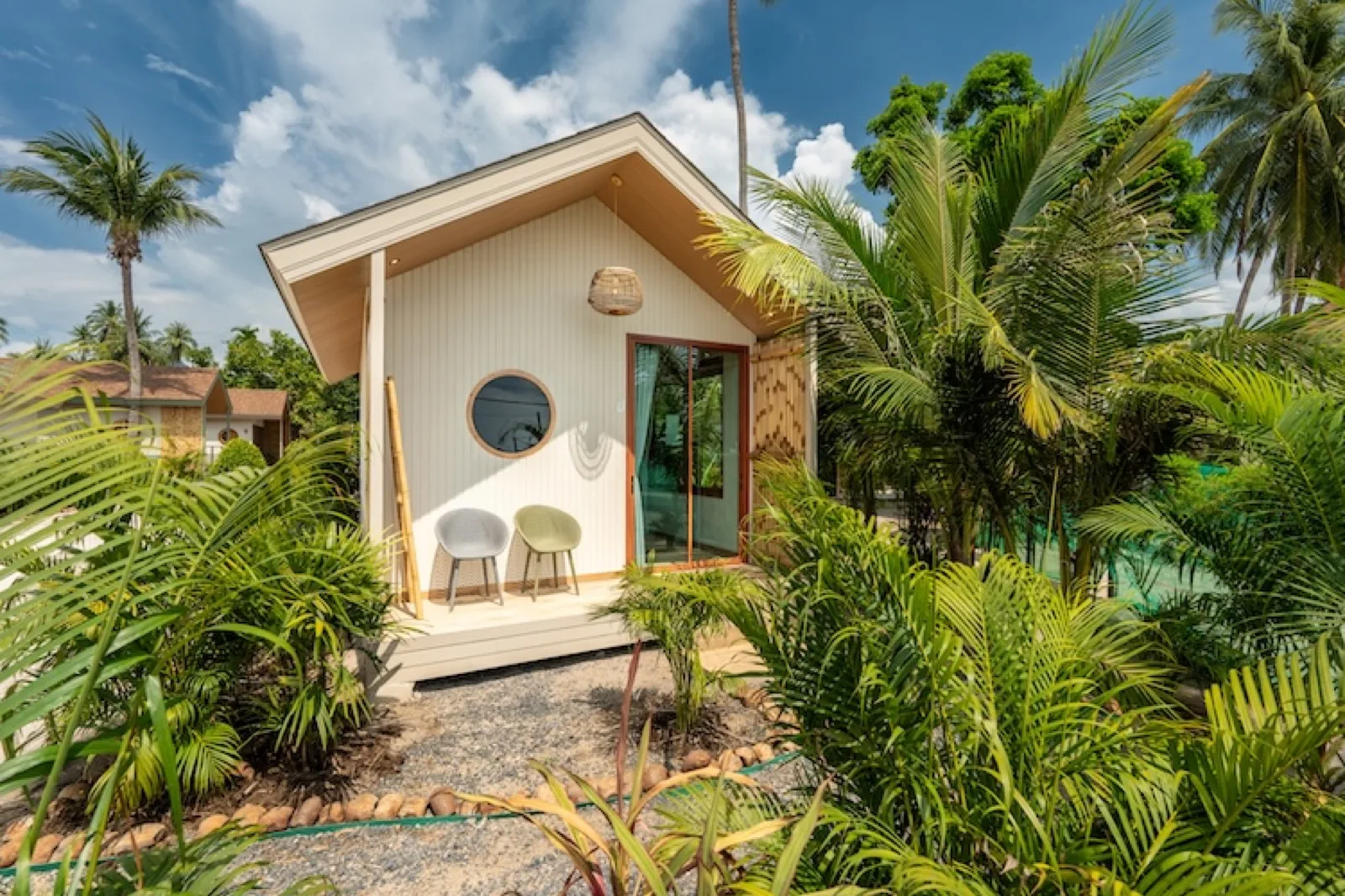 Garden bungalow with a round window among palms at Orion Healing Centre