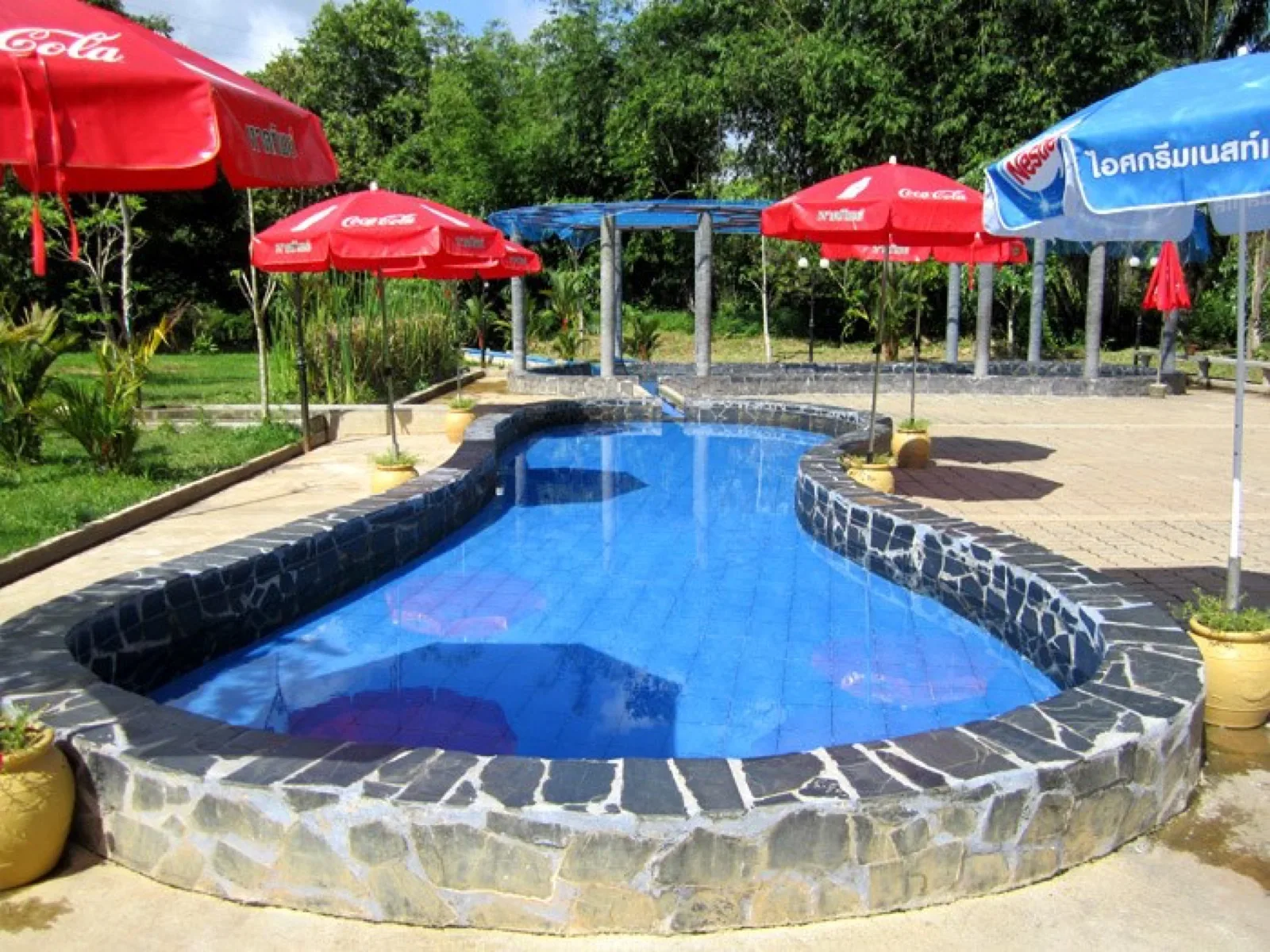 Curved open-air hot spring pool with stone edging and umbrellas at Rommanee Hot Spring