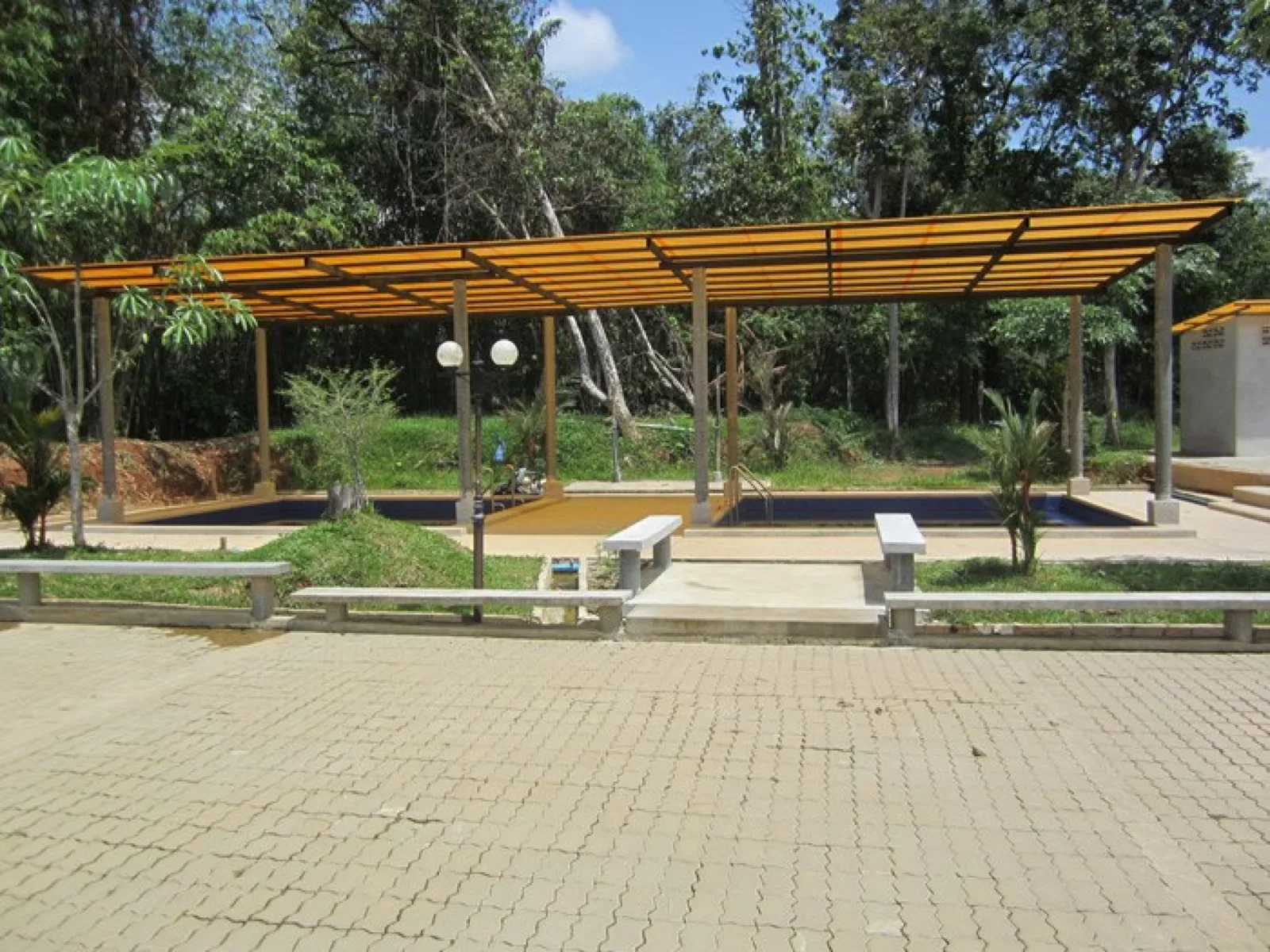 Roofed soaking pool and lawns at Rommanee Hot Spring with forested hills behind
