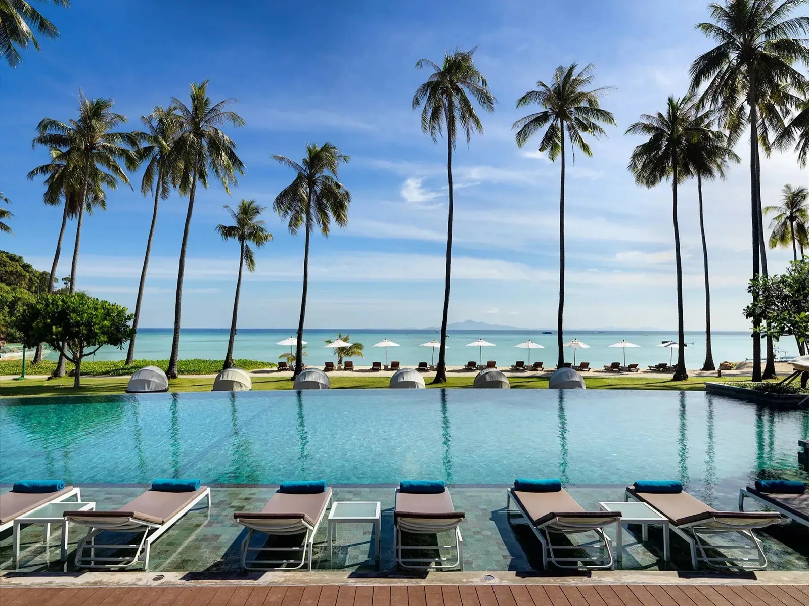 Pool lined with sun loungers and coconut palms facing the sea at SAii Phi Phi Island Village