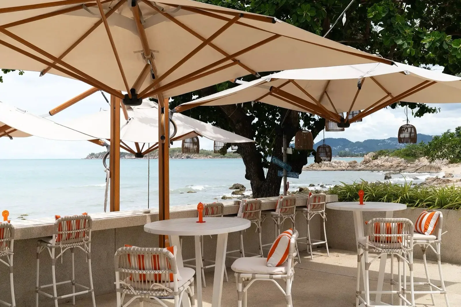Beachfront bar seating under umbrellas at SunRay Social & Swim Club, Choeng Mon