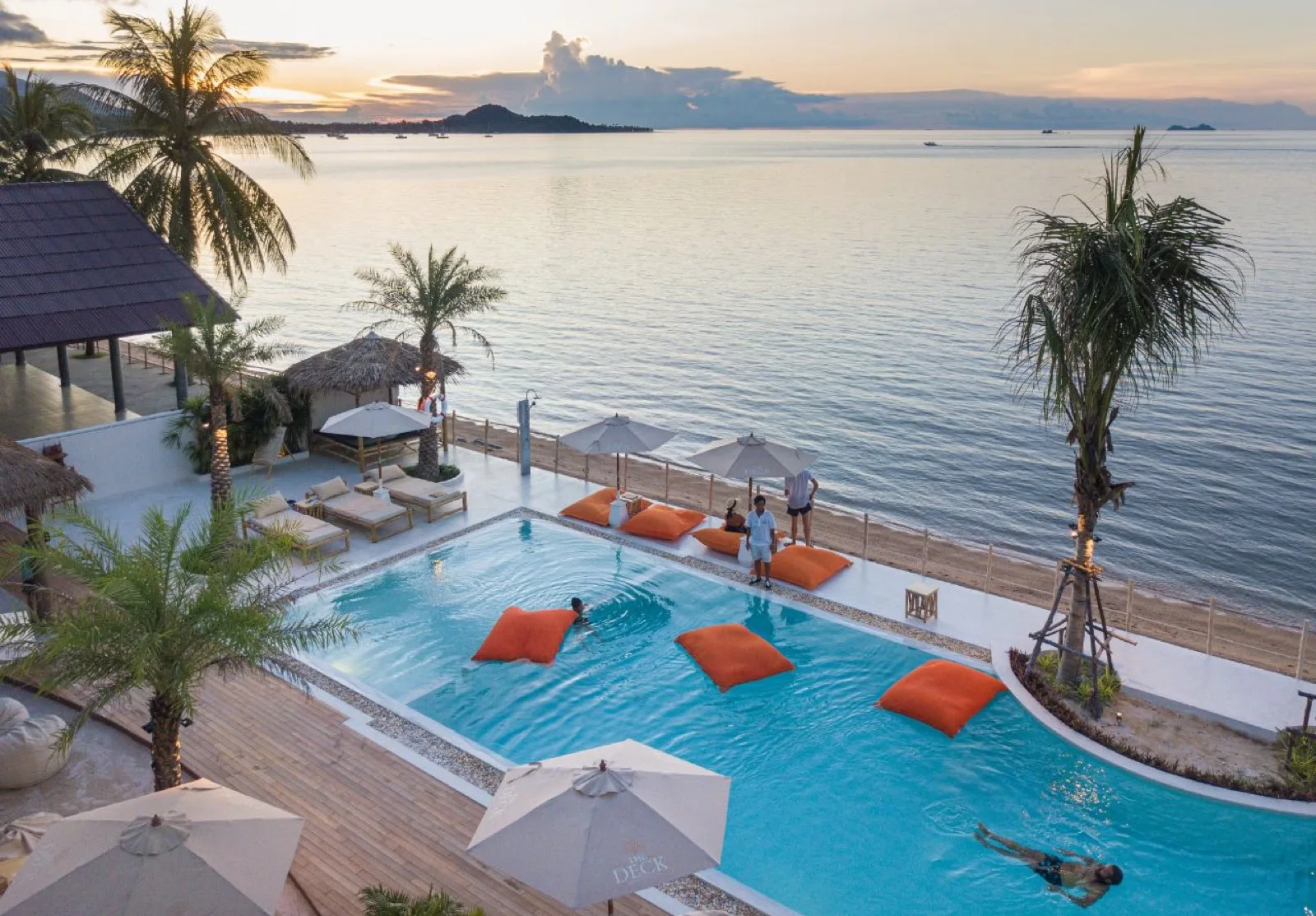 Infinity pool with orange bean bags and sea view at sunset, The Deck Beach Club Samui