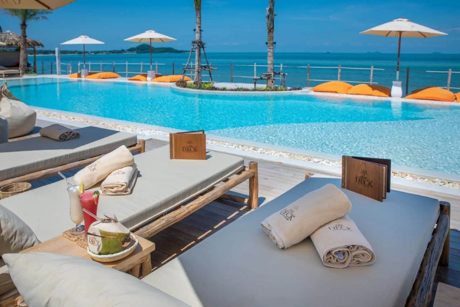 Padded poolside sunbeds with towels and umbrellas at The Deck Beach Club Samui